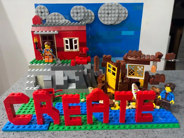 Red CREATE lettering in front of two brick-built houses, with clouds on a blue backdrop.