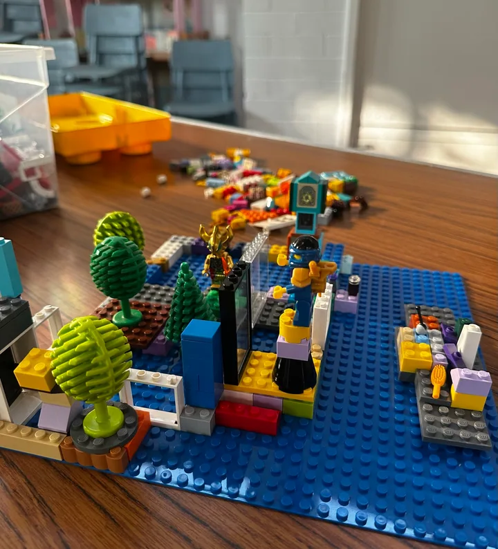 A colourful miniature scene with trees, figures and a vehicle on a blue baseplate.