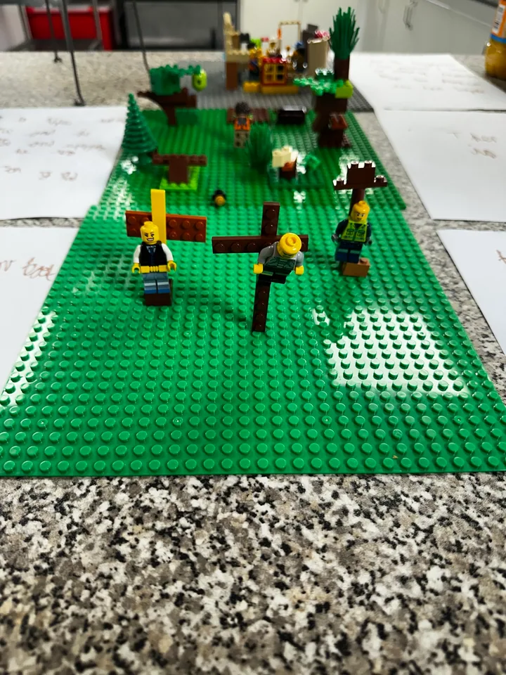A long green model with paths, trees and small figures.