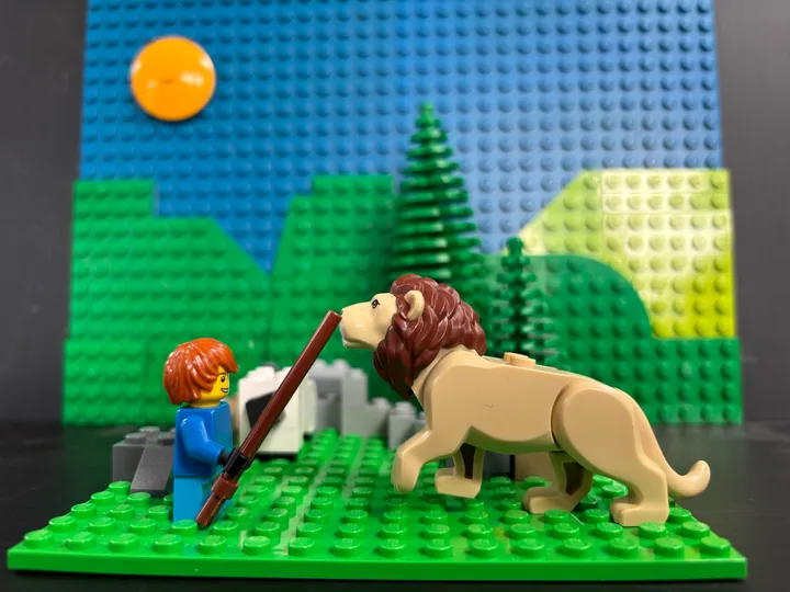 A figure facing a toy lion beneath a yellow sun and green hills made from bricks.
