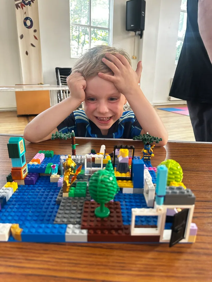 A smiling young builder behind a colourful model with trees and a blue baseplate.