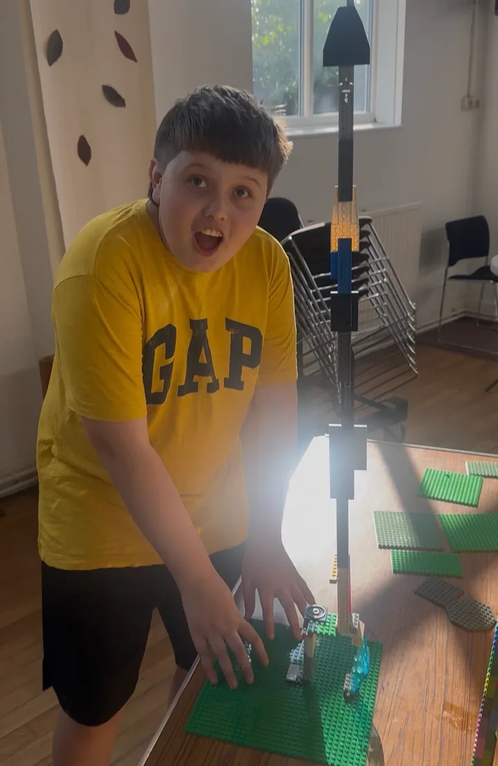 A young builder in a yellow T-shirt beside a very tall brick tower.